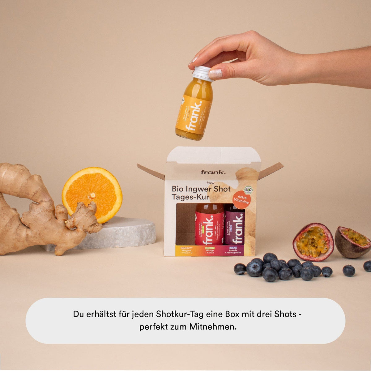 Hand nimmt einen Ingwer Shot aus der Tageskur Box mit Orange und Ingwer